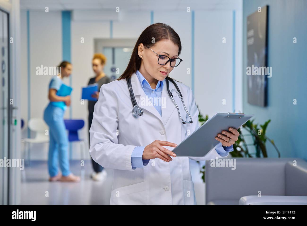Mature female doctor in white lab coat reading medical records on ...