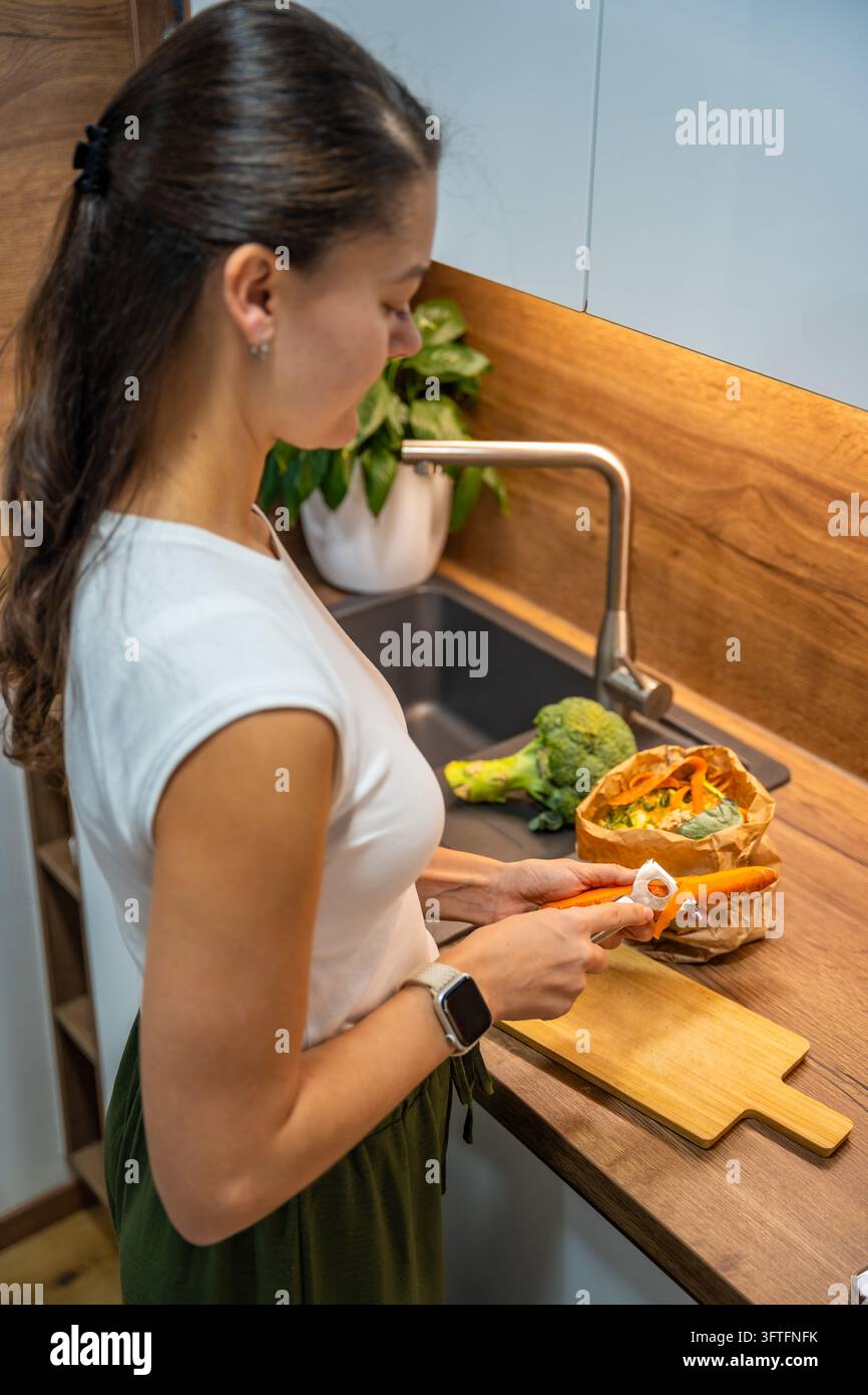 A woman prepares a carrot beside a paper bag filled with kitchen scraps ...
