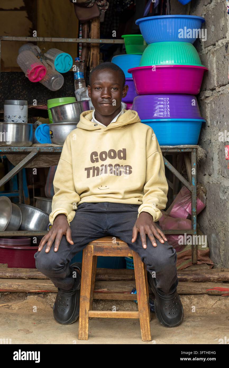 Smiling teenage boy in a beige hoodie on a stool before a shop stacked ...