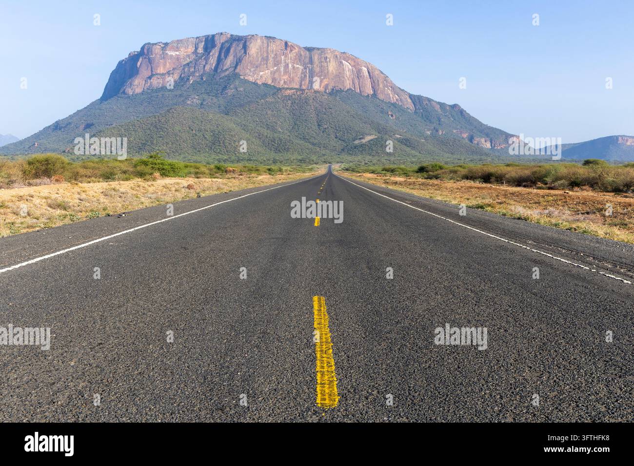 Empty asphalt road leading straight toward a large flat topped granite ...