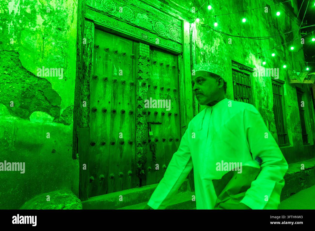 Past Papers Sign Man in a white robe and kofia carrying a paper bag past an old carved ...