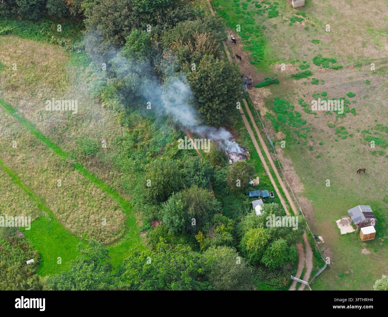 Aerial view of a small fire burning near a line of trees in a rural ...