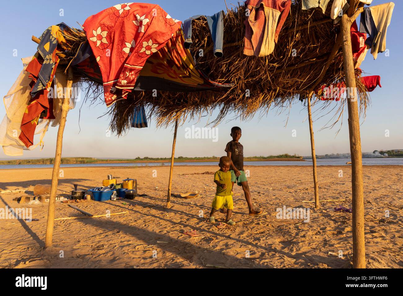 Smiling boy holding a small chick in his hands beside a riverside camp ...