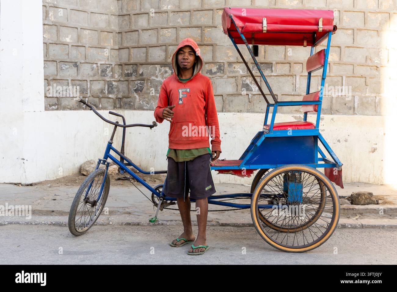 Young man wearing a hooded sweatshirt standing beside his blue bicycle ...