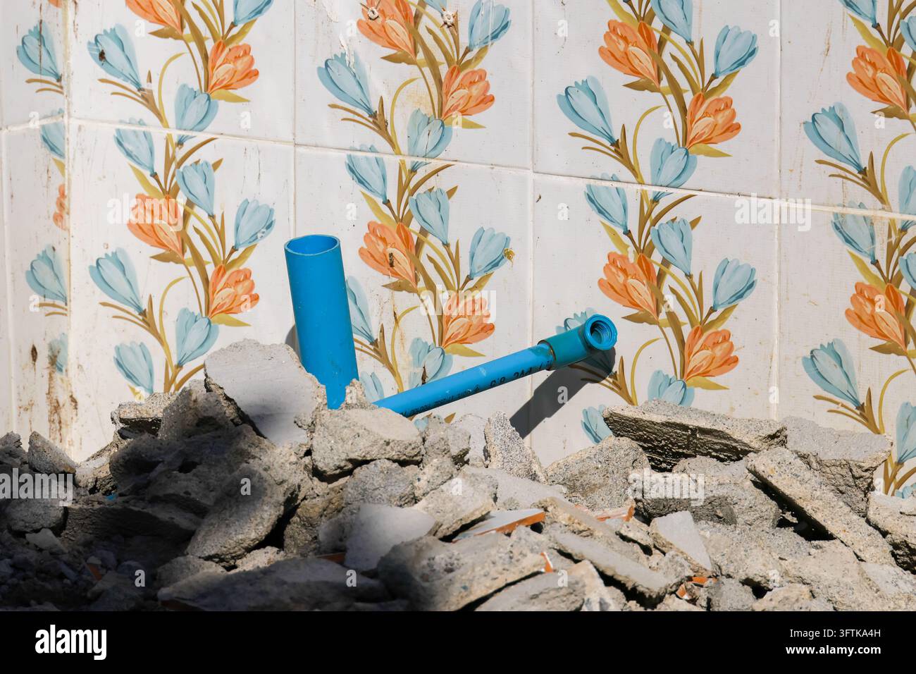 A colorful ceramic wall tile with floral pattern behind broken concrete ...