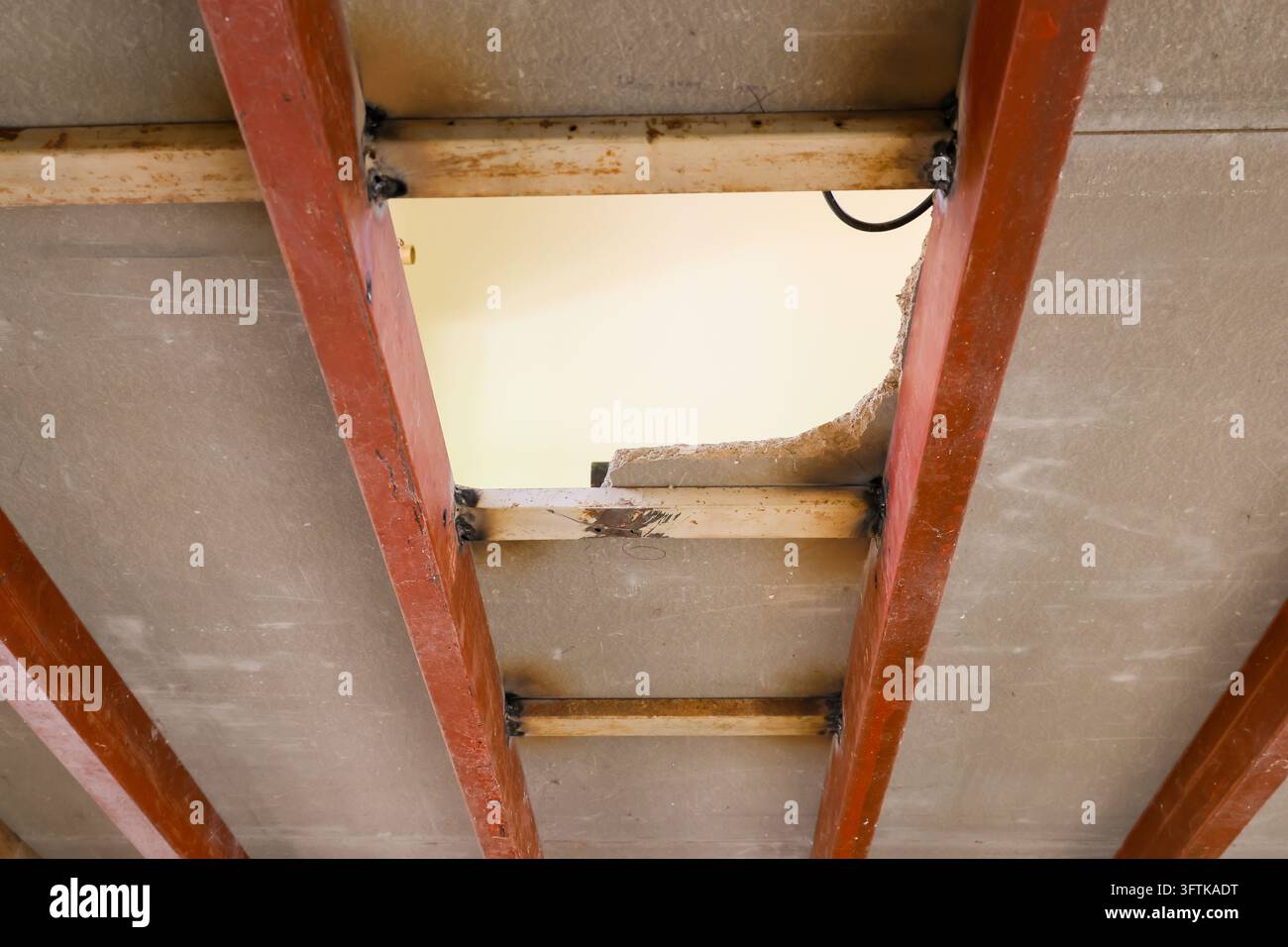 A damaged ceiling panel showing exposed roof framing, rusted metal ...