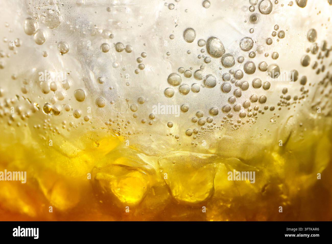 A golden carbonated beverage with rising bubbles and ice, photographed ...