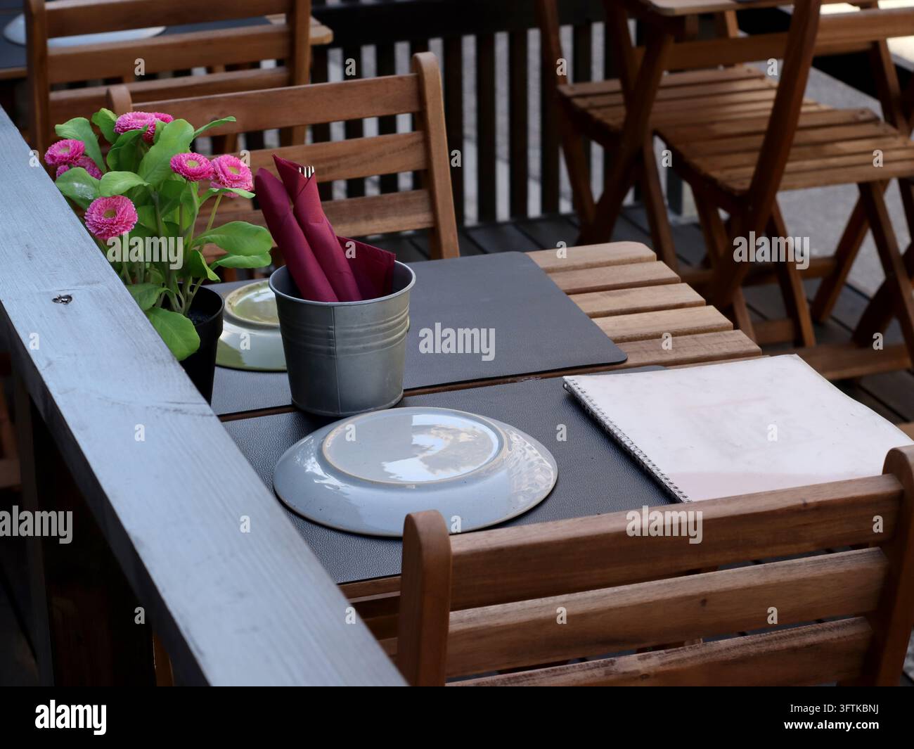 Using A Pink Flower Outdoor cafe table with wooden chairs, empty plates, red napkins and a ...