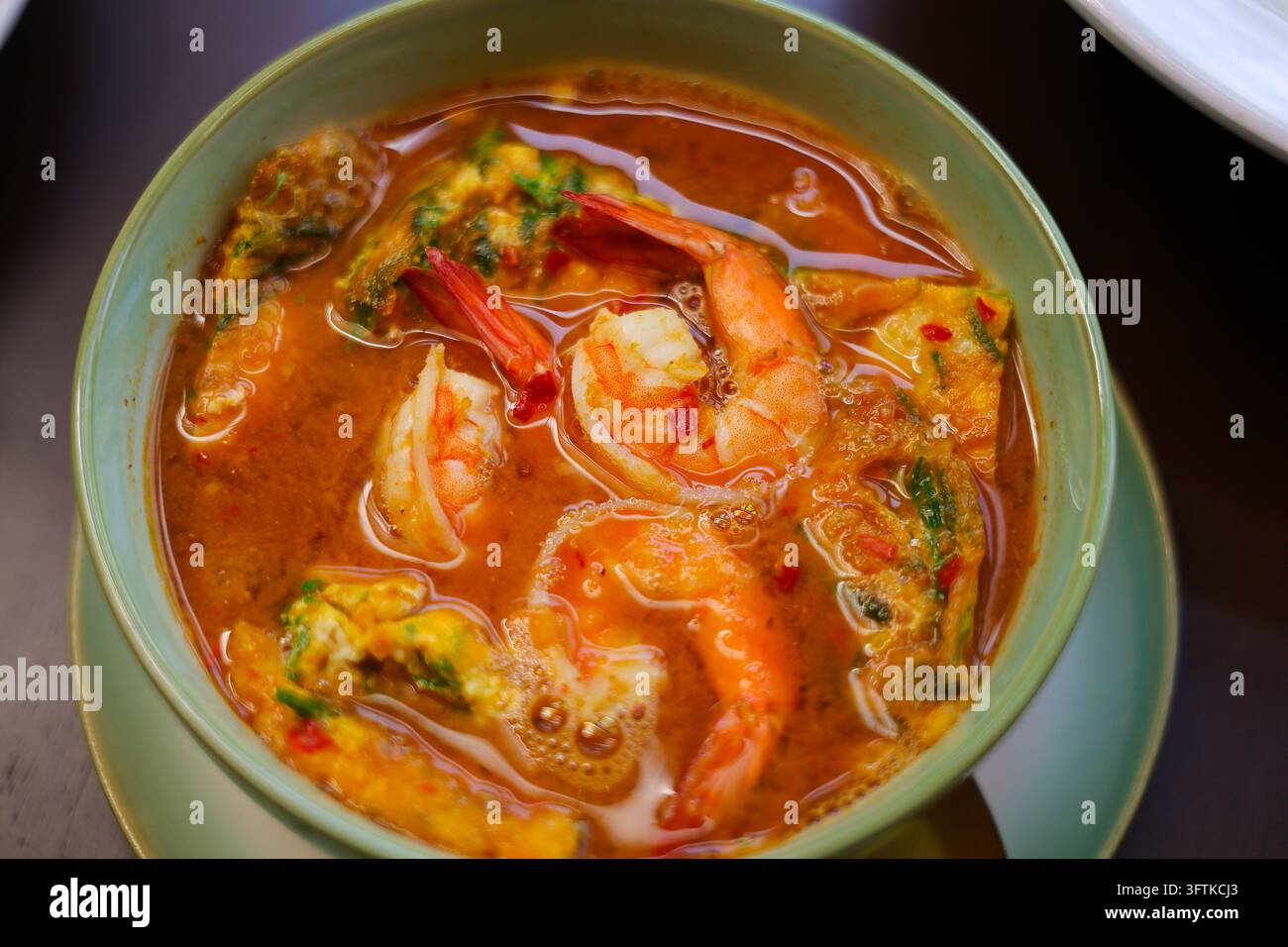 A spicy shrimp soup served in ceramic bowl with herbs, vegetables, and ...