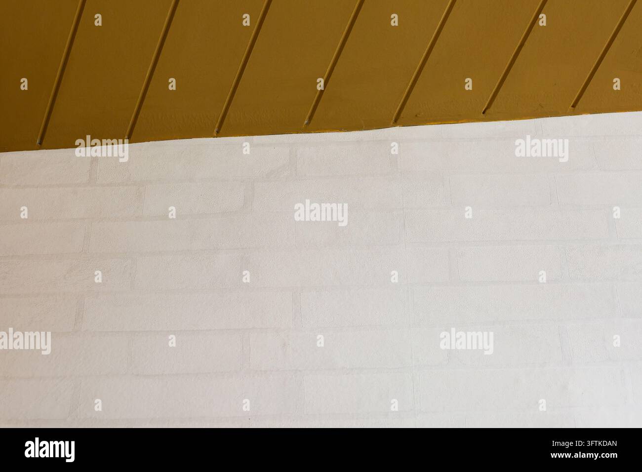 A white brick wall beneath brown sloped ceiling, minimal architectural ...