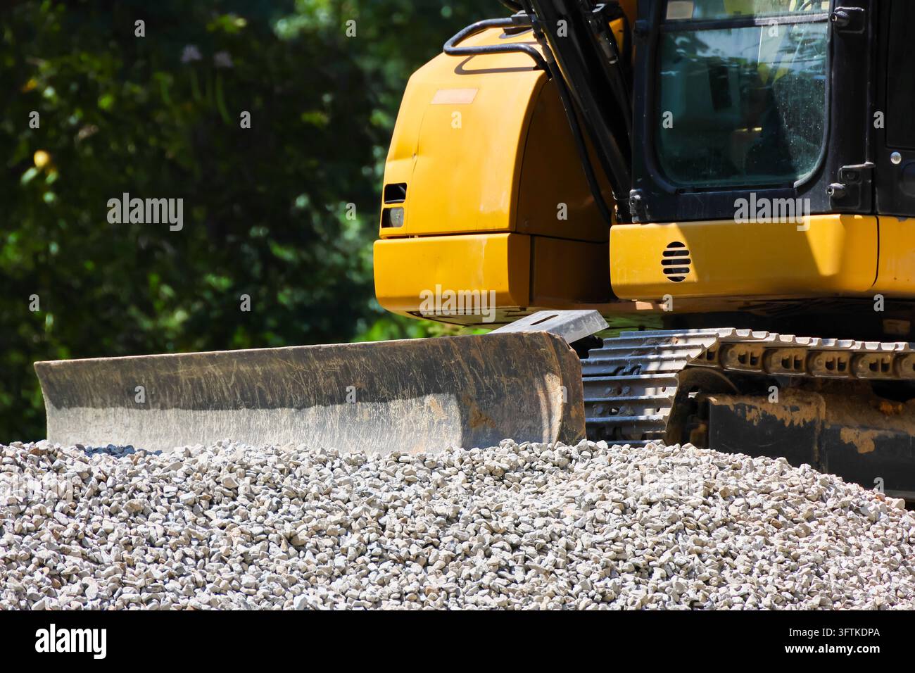 A yellow excavator with blade beside pile of crushed stone at ...