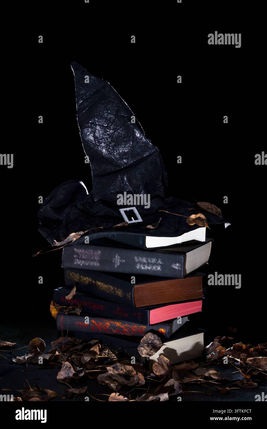 Black witch hat on a stack of books surrounded by leaves against a ...