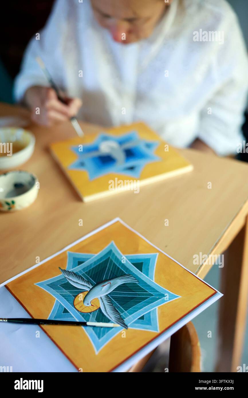 An artist is meticulously working with a fine brush on a religious icon ...
