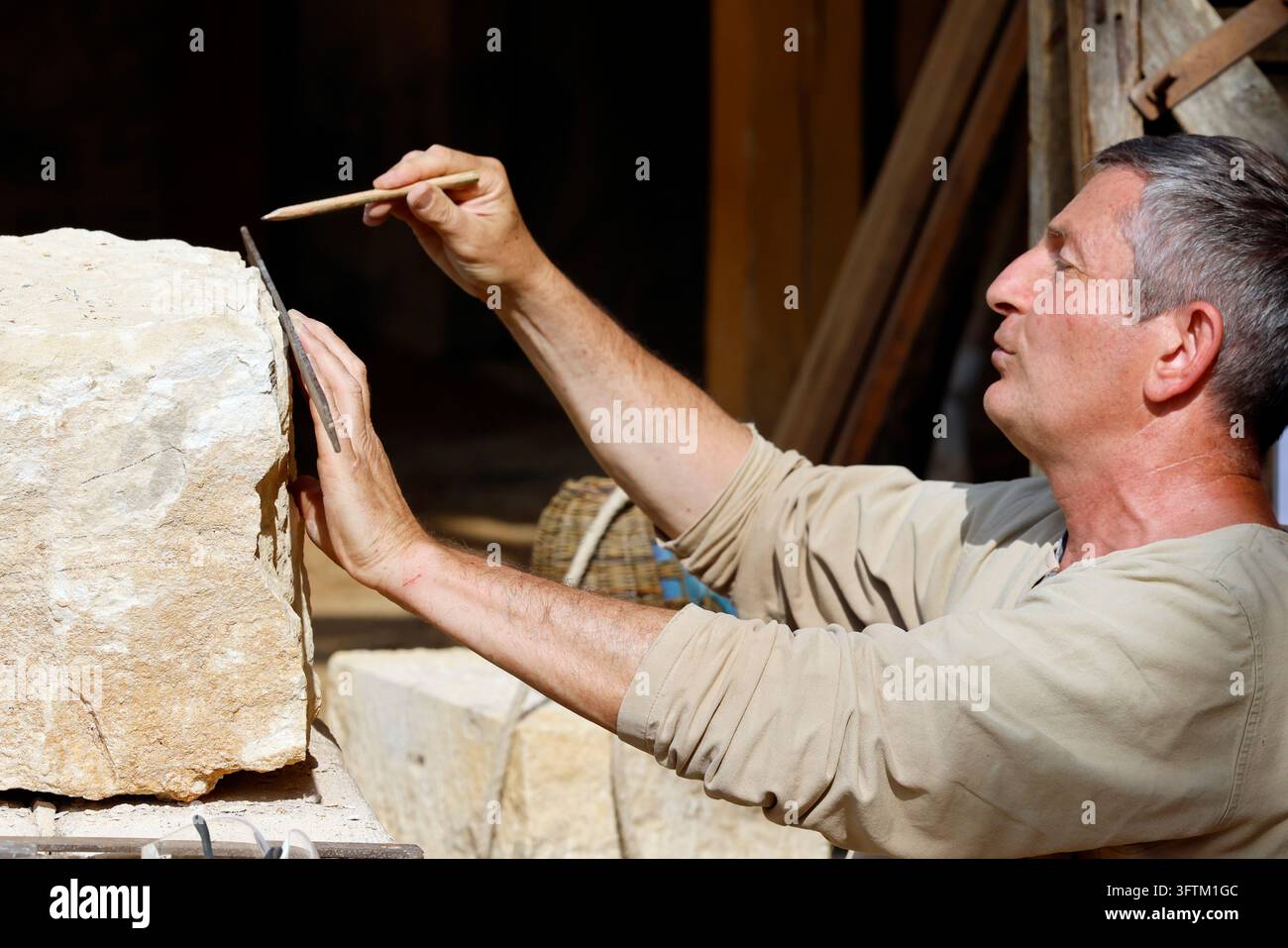 A stonemason carefully measures a block of light-colored limestone ...