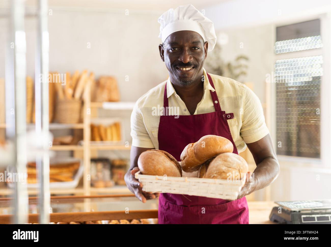 Portrait of positive male baker with bread and baguettes in hands in ...