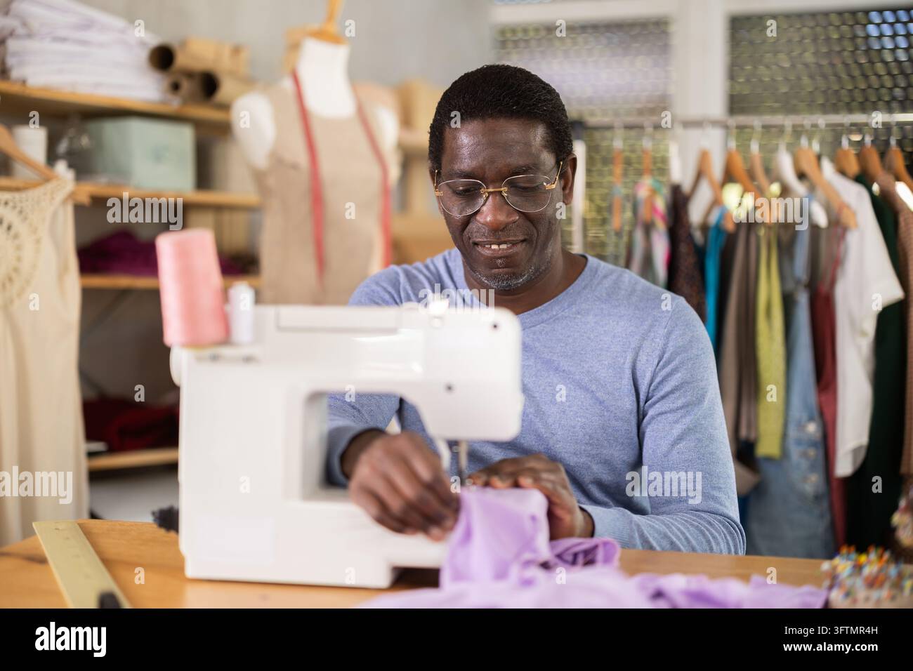 In workshop, African American man employee works with sewing machine ...