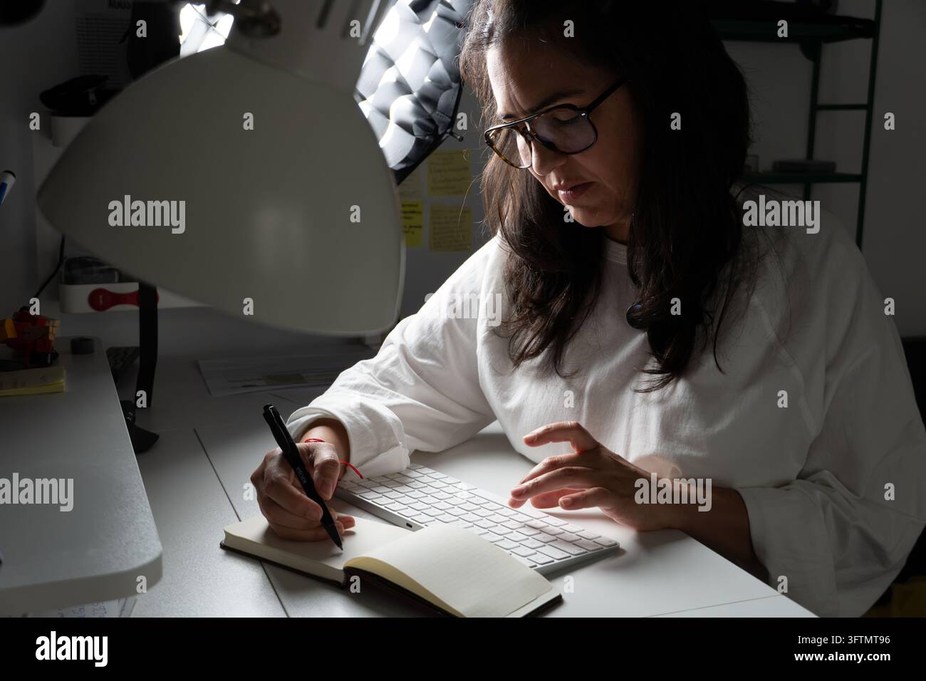 Woman focusing on work, writing notes in a small book while also using ...