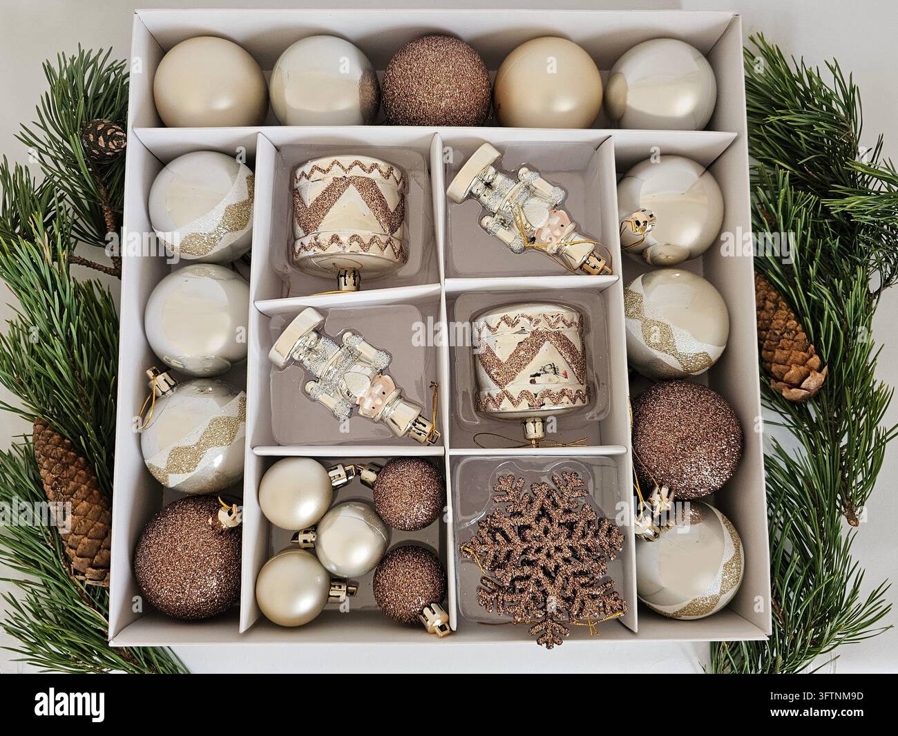 Top view of an open box filled with elegant Christmas tree ornaments in champagne, ivory and rose gold tones. Decorative baubles, nutcracker figures, drums and a glittering snowflake. Stock Photo
