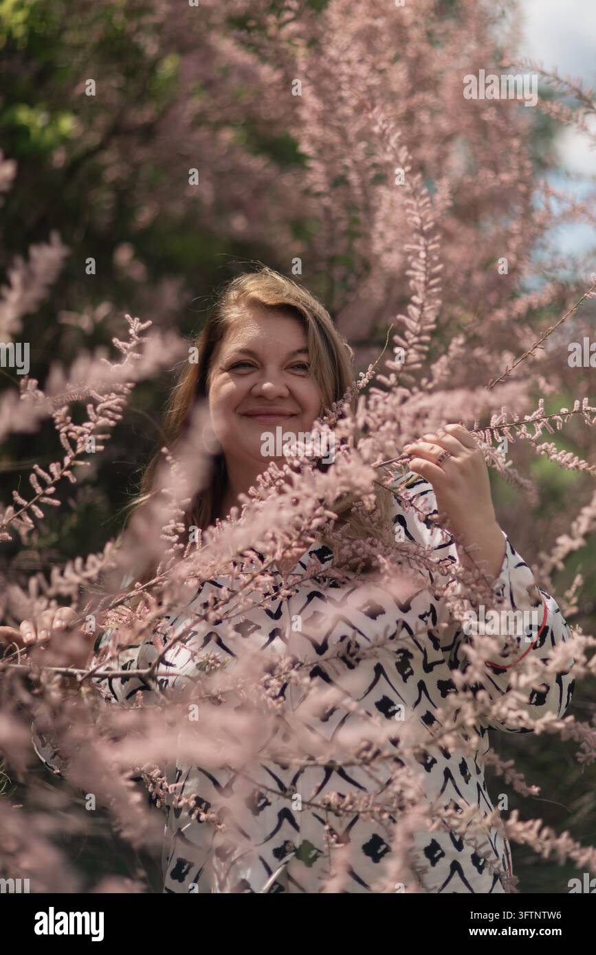 Using A Pink Flower Close-up portrait of a smiling mature woman standing amongst dense pink ...