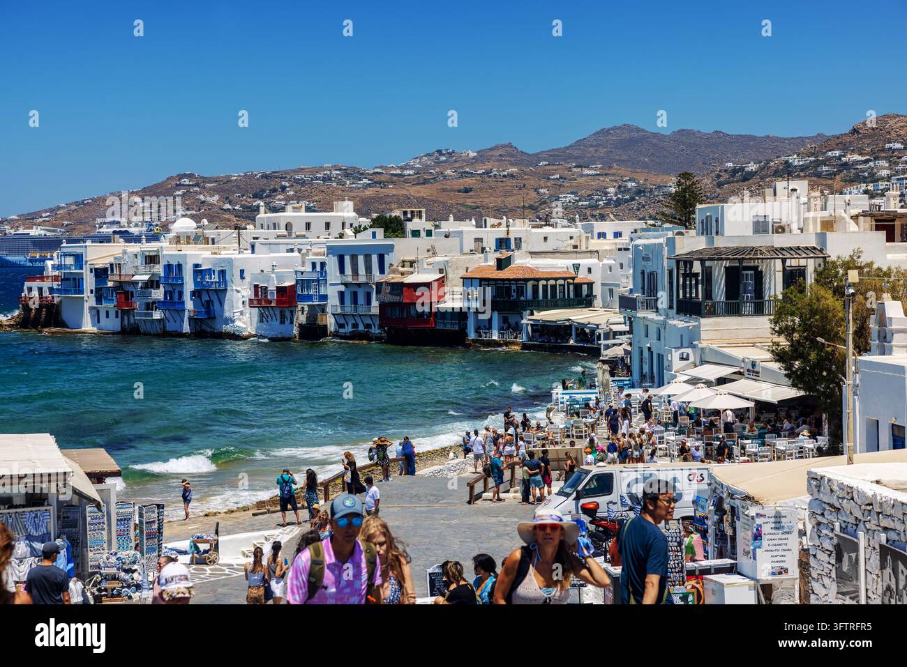 Mykonos, Greece - July 16, 2026: Visitors walk along the waterfront of ...