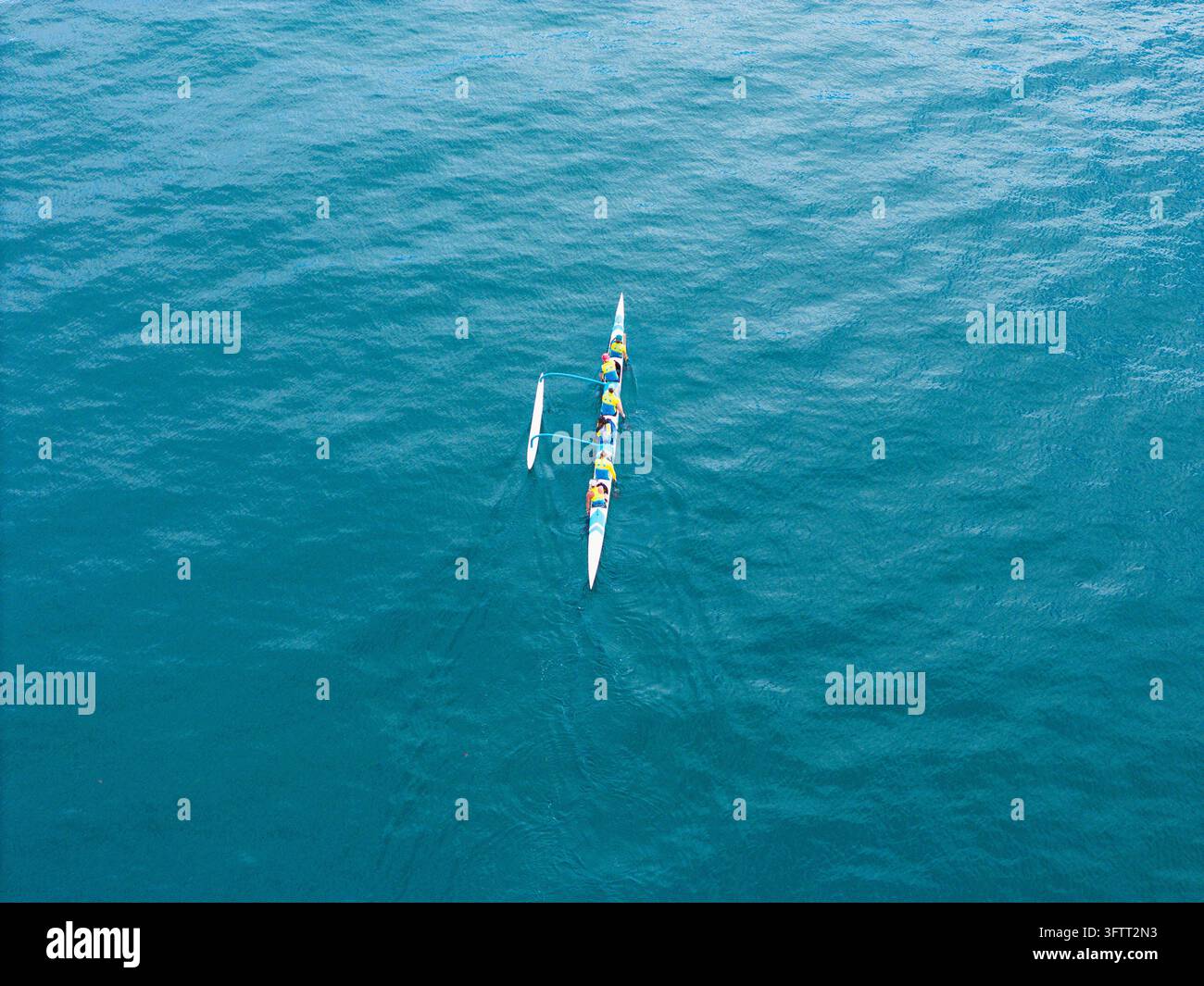 Canoe In Ocean Aerial view of an outrigger canoe with people paddling across the blue ...