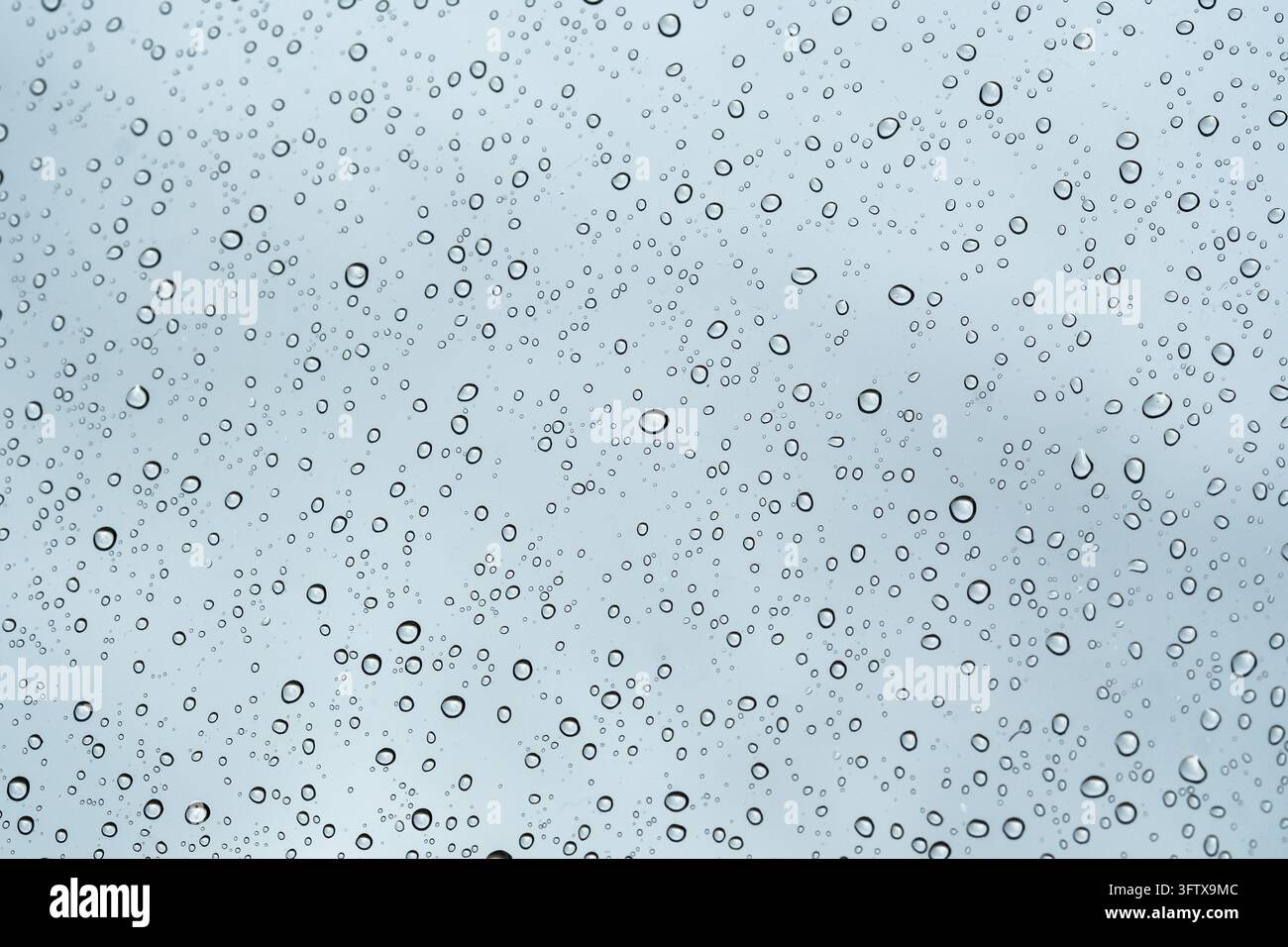 Raindrops falling and trickling down window glass on blue background Stock Photo