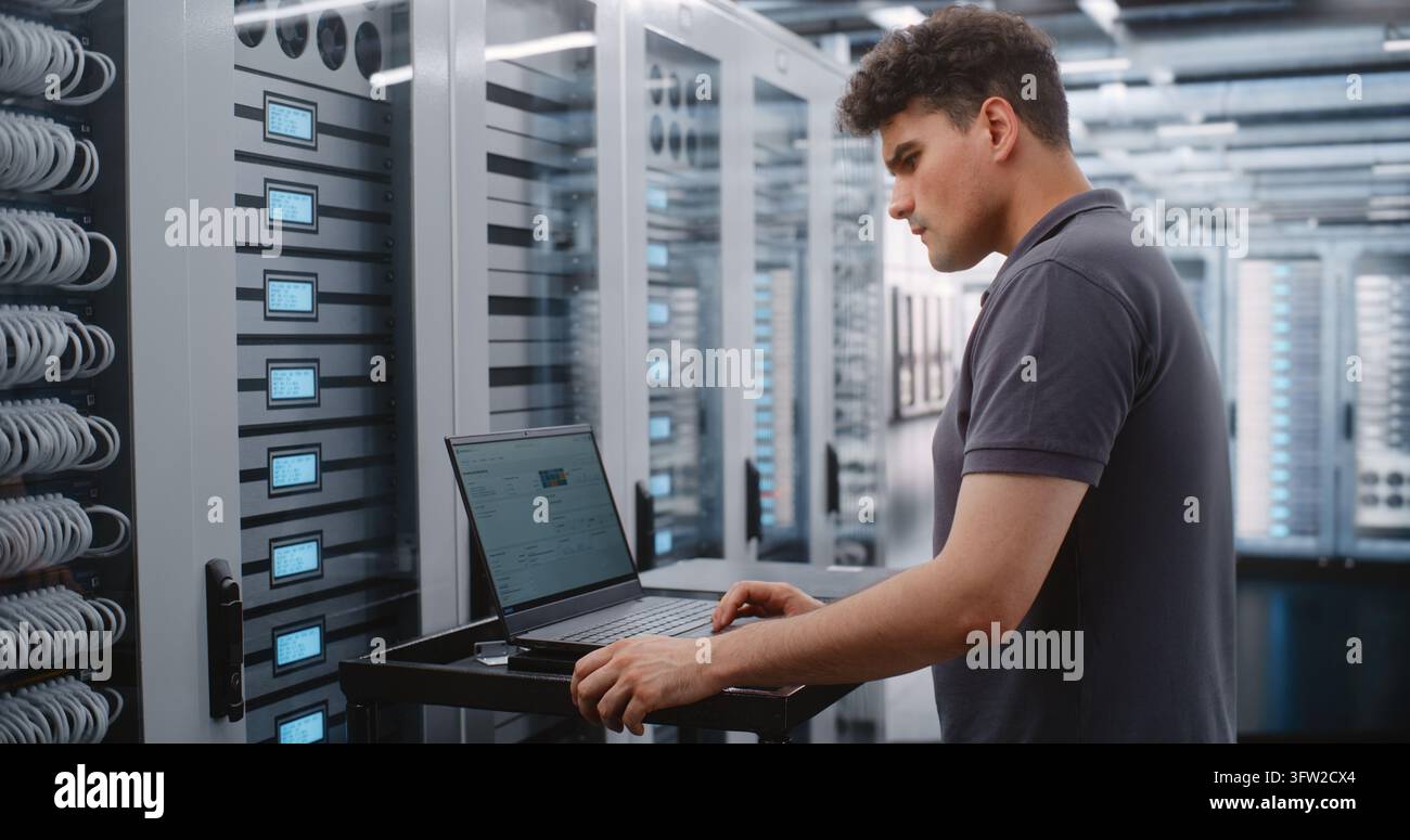 Male System Administrator Analyzes Server Telemetry on Laptop While Female Engineer Works on Nearby Racks, Combining Software Diagnostics with Physical Infrastructure Inspection inside Modern Data Center. Stock Photo
