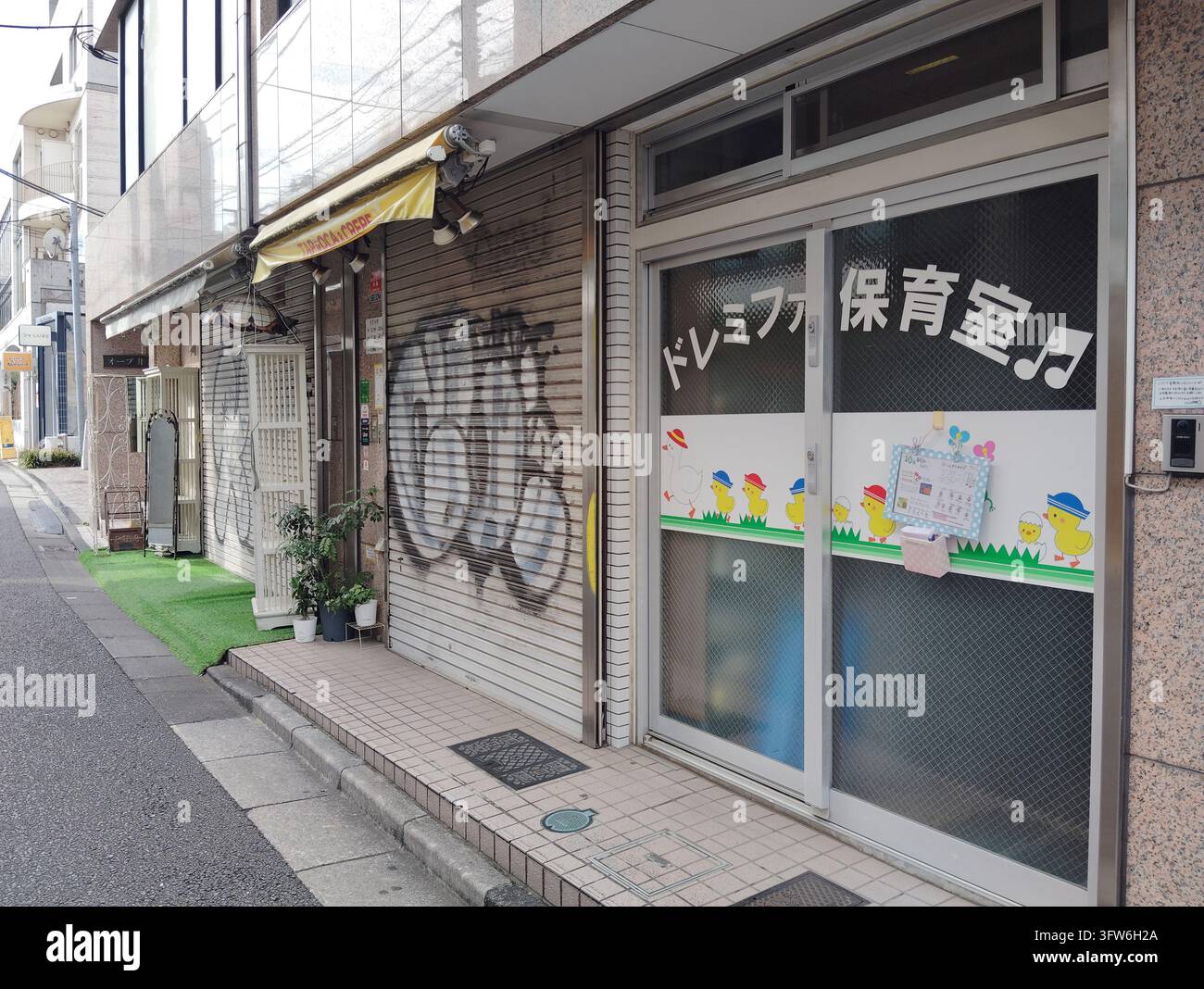 Nursery entrance beside a graffiti-covered shop shutter on a street in Tokyo, Japan. - Smartphone Captured Stock Image