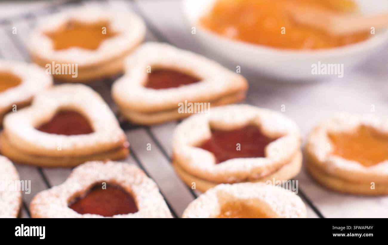 A close-up shot captures star and heart shaped Linzer cookies filled with sweet jam and dusted with powdered sugar on a wire rack under soft natural l Stock Photo