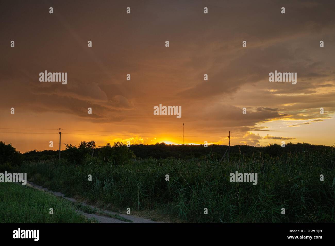 Dramatic Orange Sunset Beneath Dark Clouds Over a Rural Landscape Stock Photo