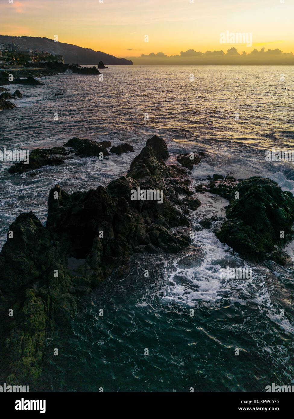 A vertical view from above displaying dark rugged coastal rocks with ...