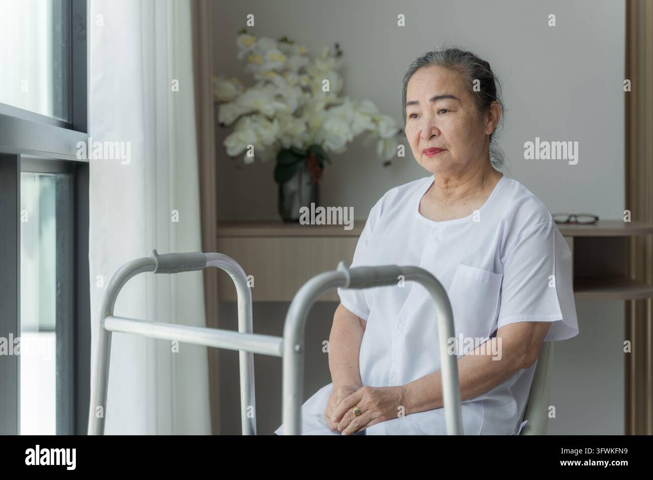 Senior woman using a walker while sitting at home, reflecting on her ...