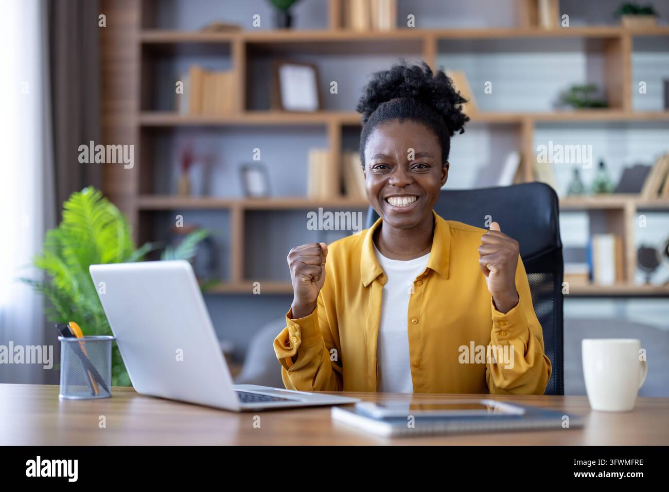 Cheerful woman at desk with laptop gives upbeat thumbs-up in bright ...
