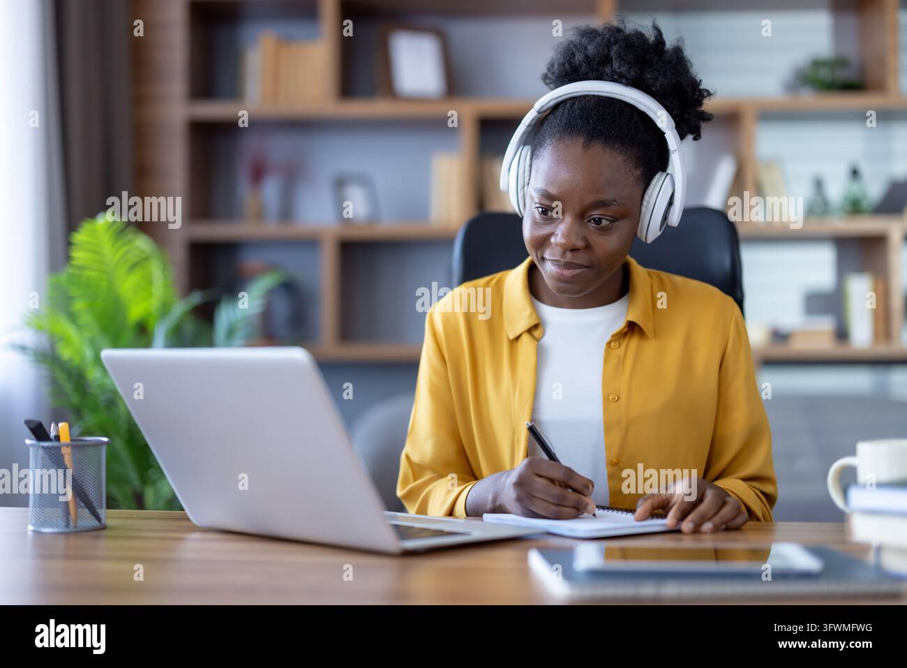 Young professional woman wearing headphones writes in notebook beside ...
