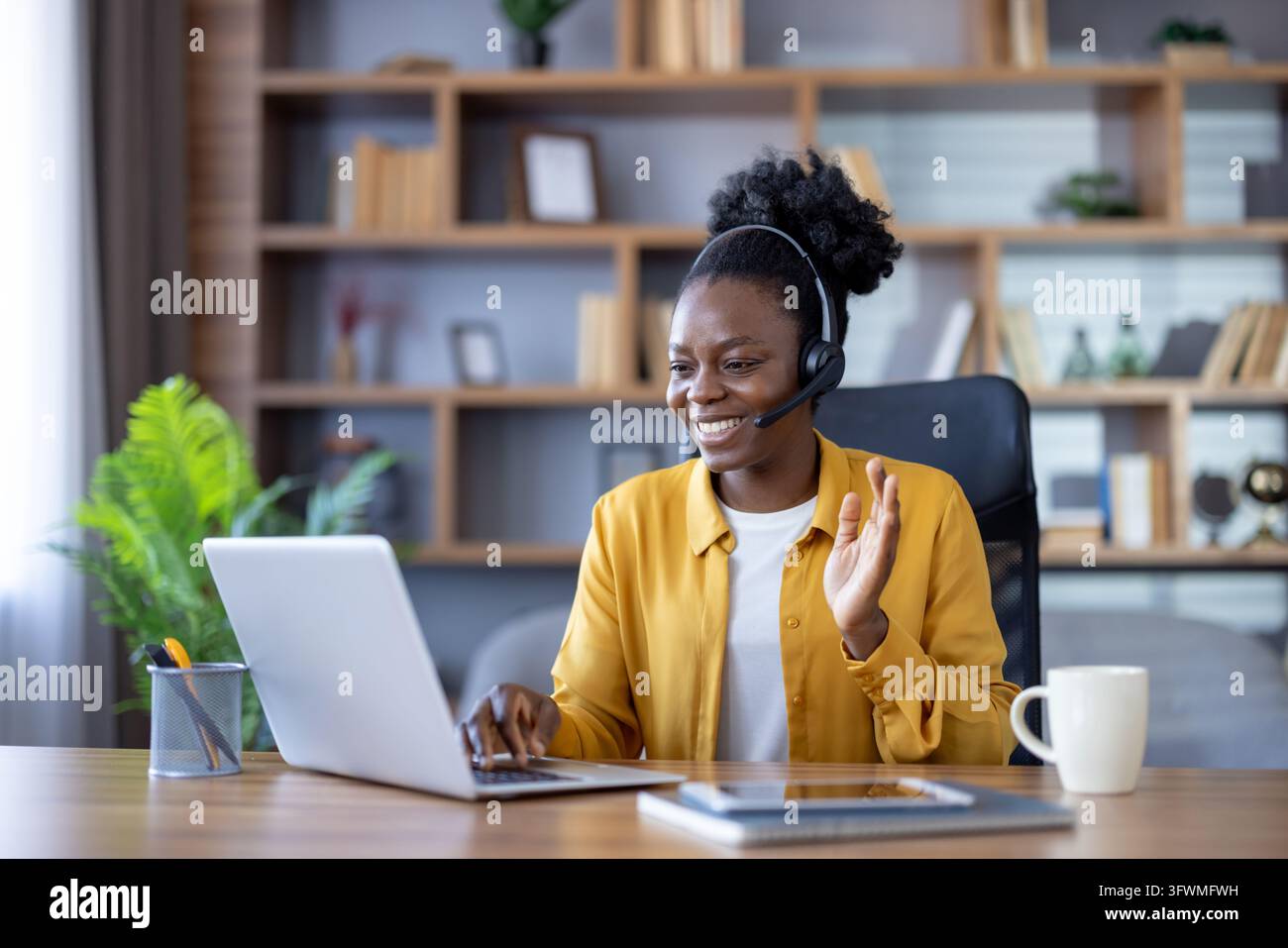 Friendly woman in headset works at laptop and greets client from modern ...