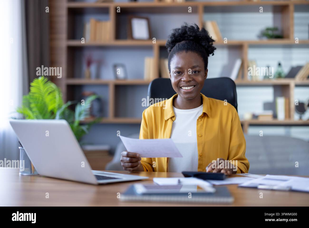 Smiling businesswoman holds documents at desk with laptop in bright ...