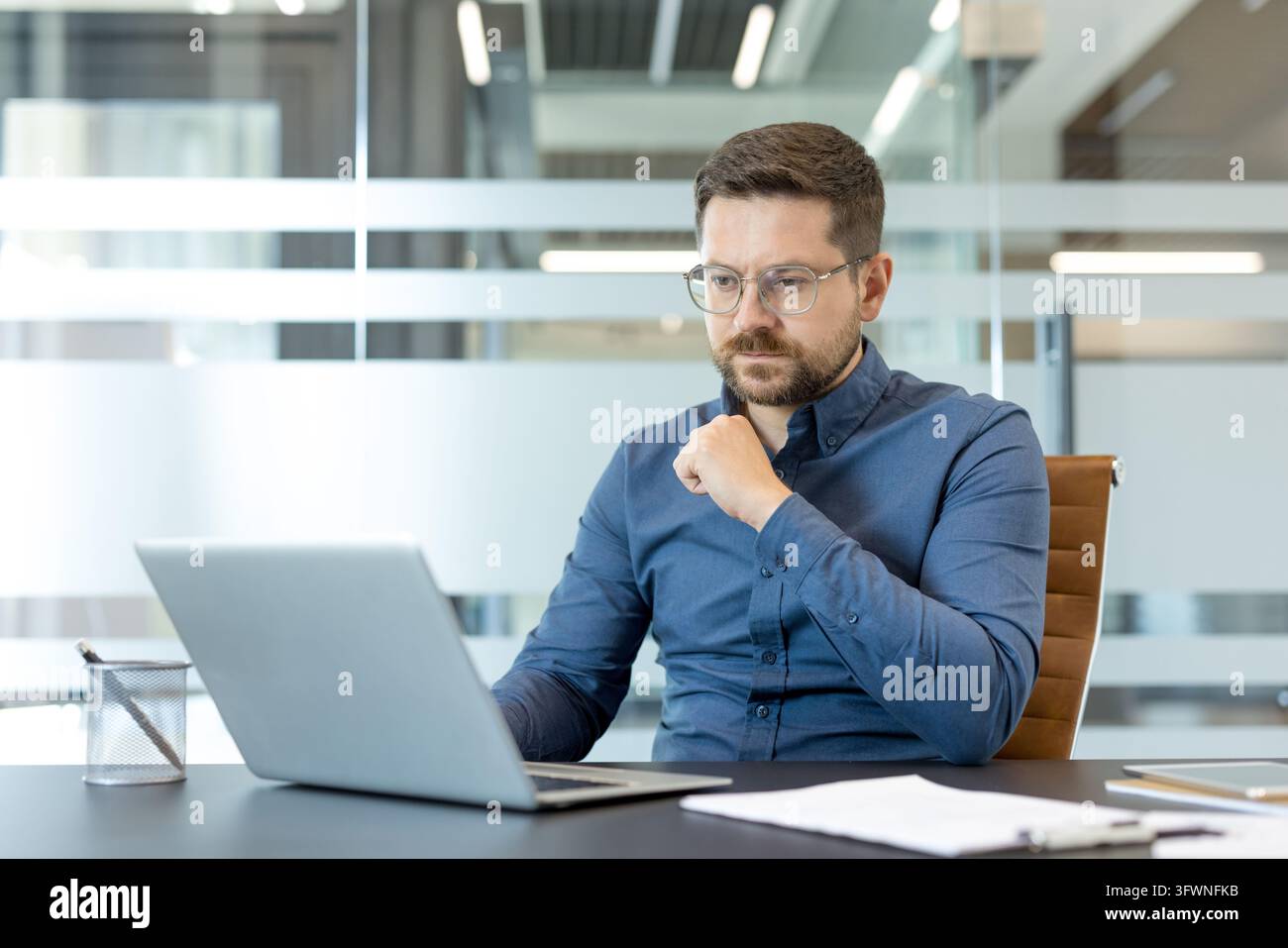 Serious office professional studies information on laptop at desk, with ...