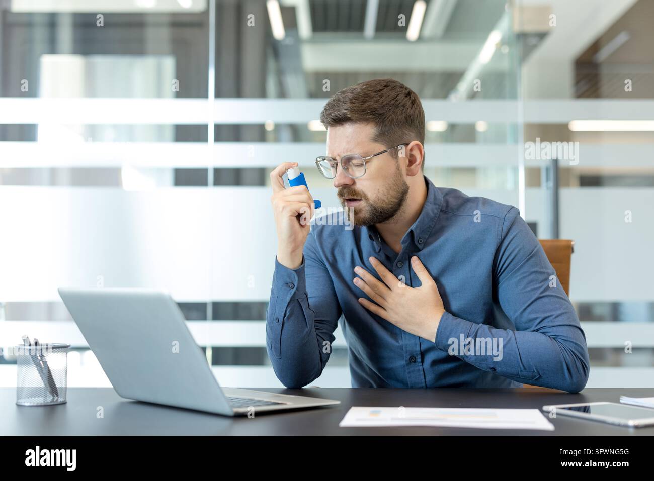 Young professional sits at desk in modern office, using inhaler while ...