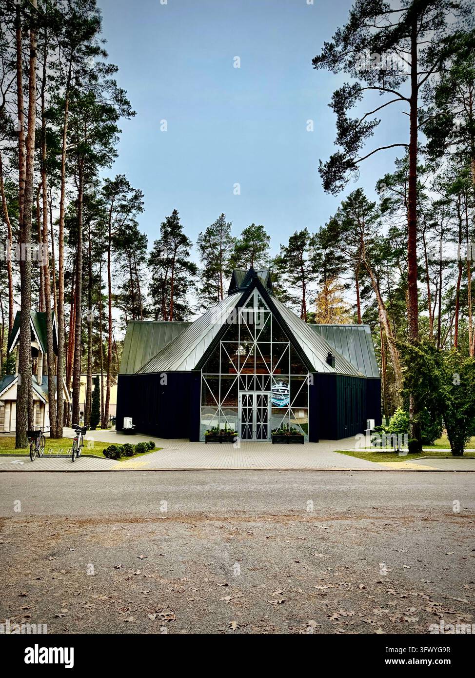 A vertical photograph capturing the modern Church of the Blessed Virgin Mary, Mediatrix of All Graces in Kulautuva, Lithuania, surrounded by tall pine - Smartphone Captured Stock Image