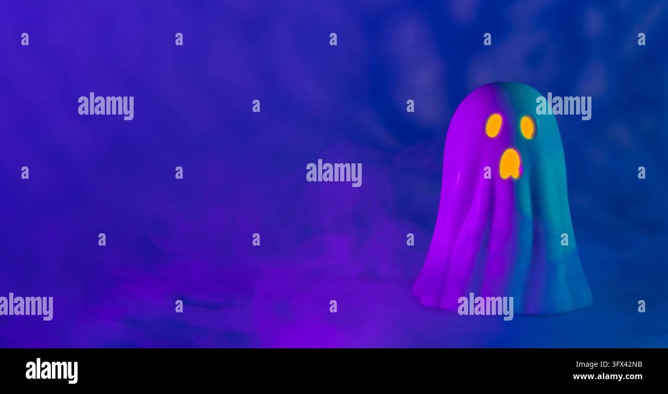 Front view of a white ceramic ghost with purple and cyan light, its face illuminated in yellow, set against a blue background with dark blue shadows a Stock Photo