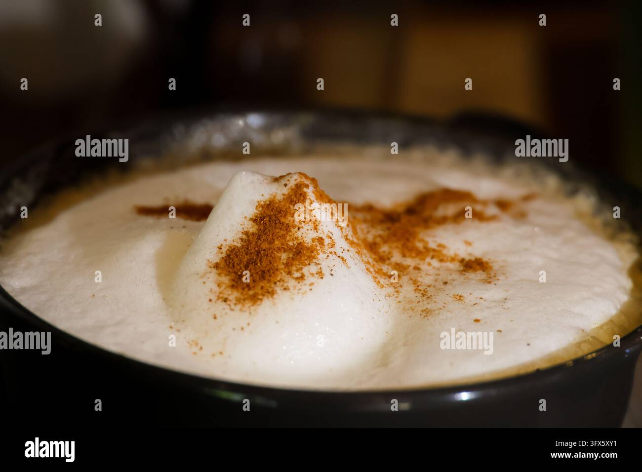 A cappuccino with frothy milk and cinnamon powder in dark ceramic cup ...