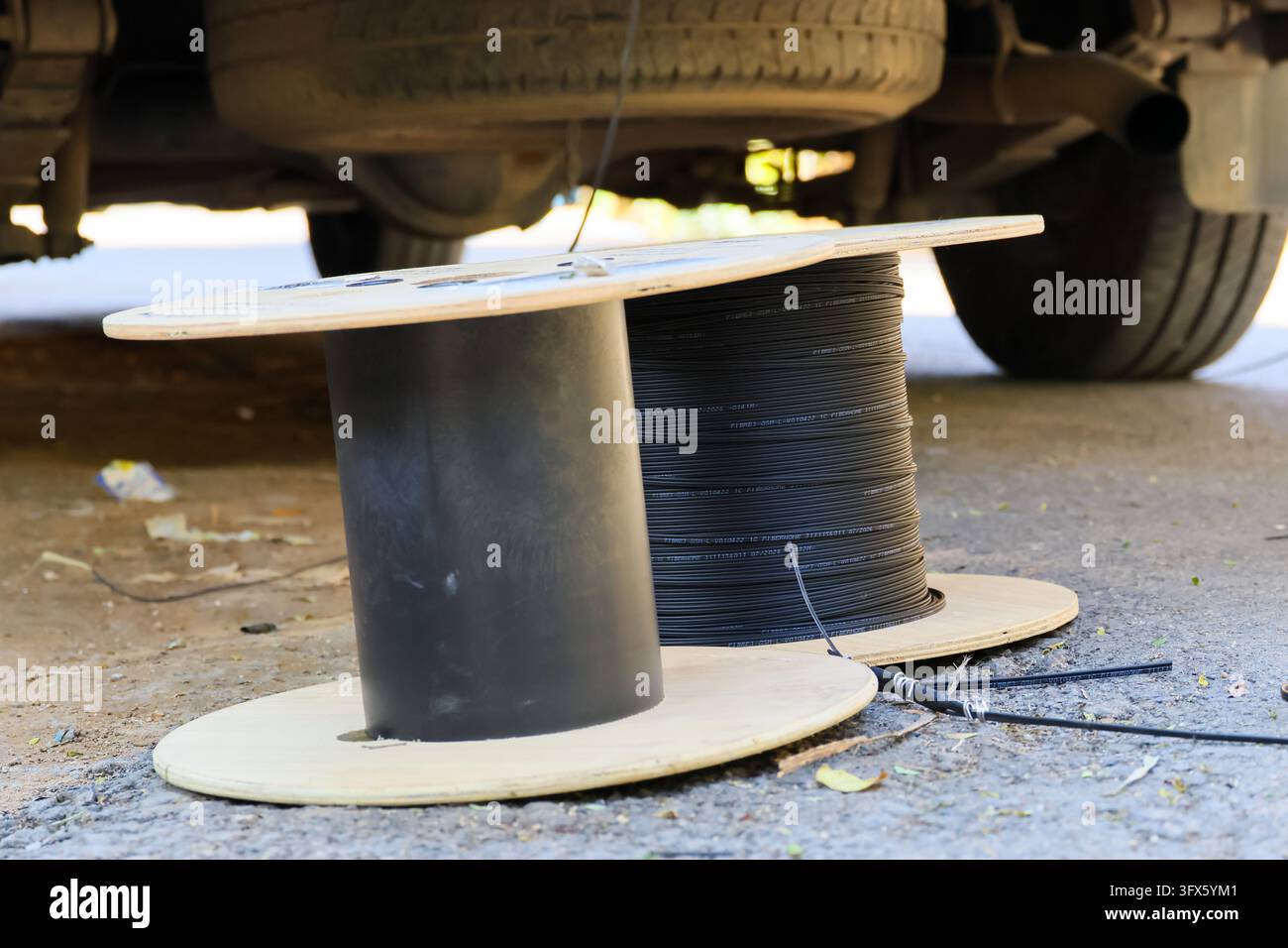Spool Phot A fiber spool holding black cable beneath parked vehicle, with wooden ...