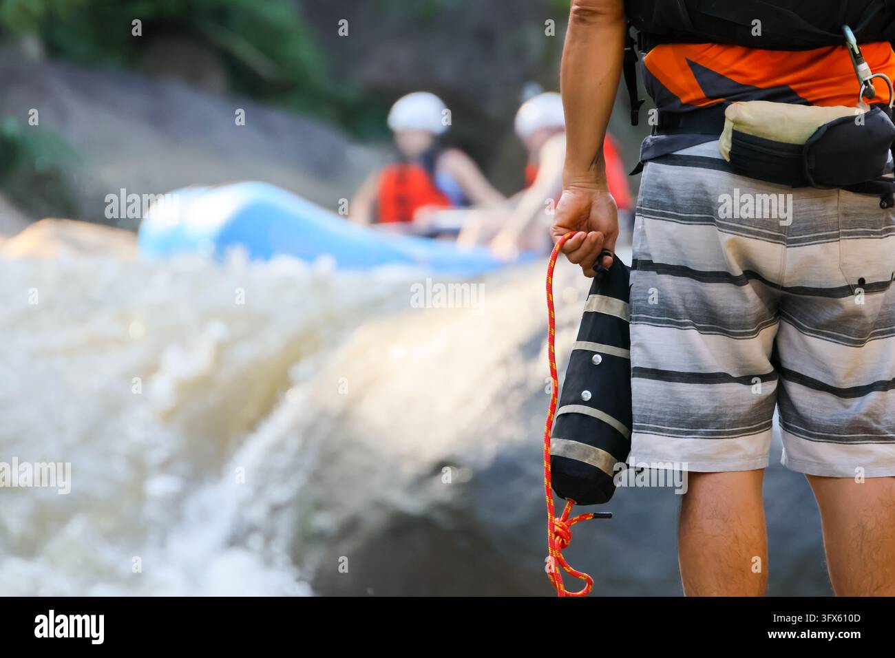 A rafting guide holding safety rope beside rushing river rapid, with ...