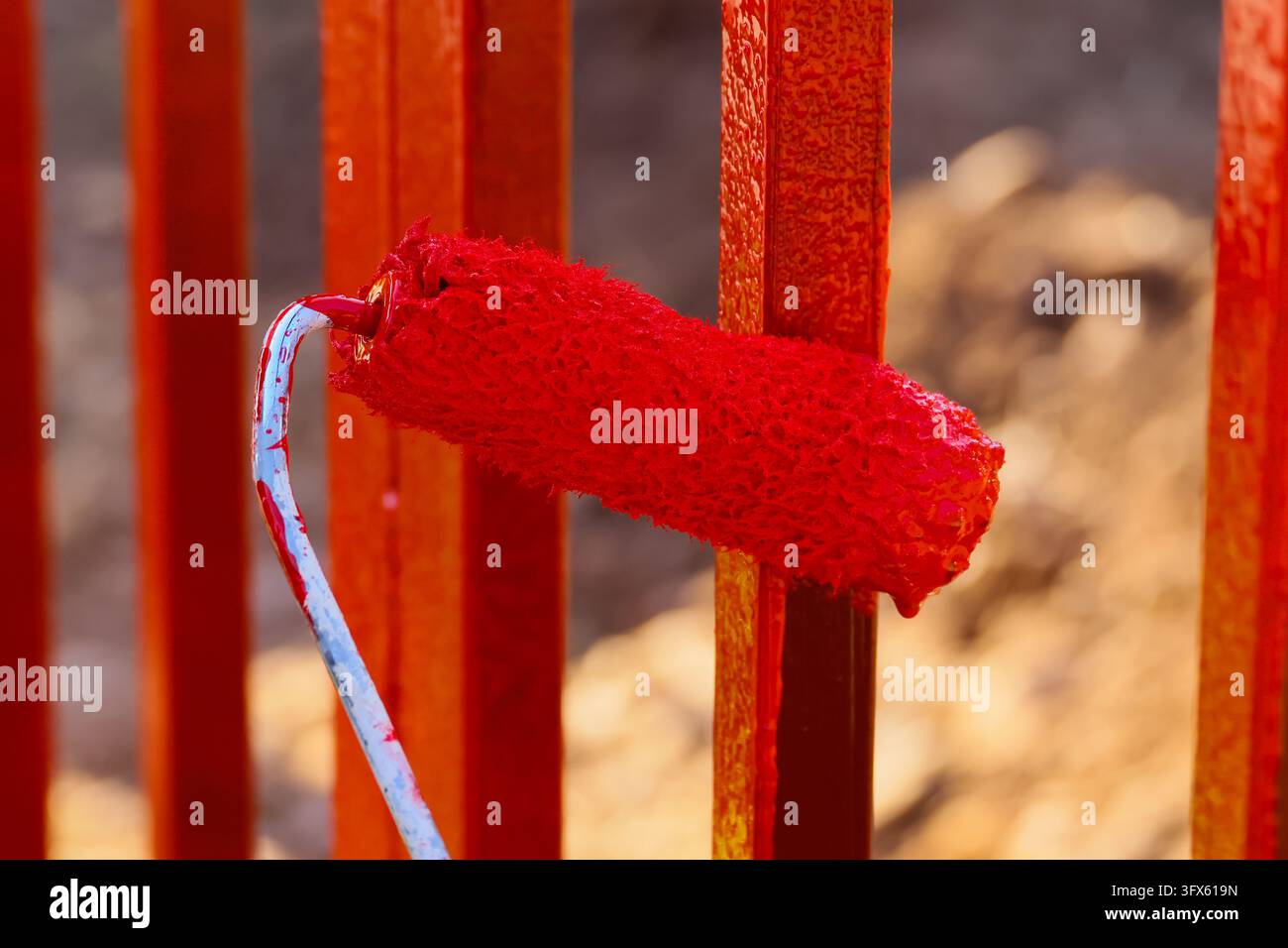 A red paint roller beside metal fence creating vivid color contrast in ...