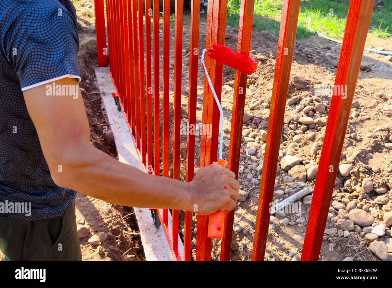 An unidentified worker paints red metal fence beside concrete base and ...