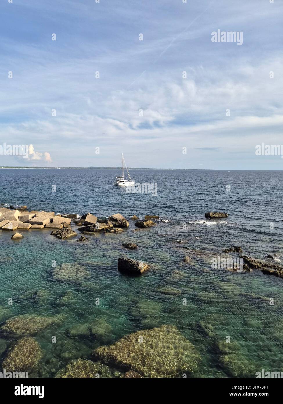 Clear turquoise sea over limestone rocks with a sailboat on the horizon, Gallipoli, Salento, Apulia, Italy, September 2026 - Smartphone Captured Stock Image