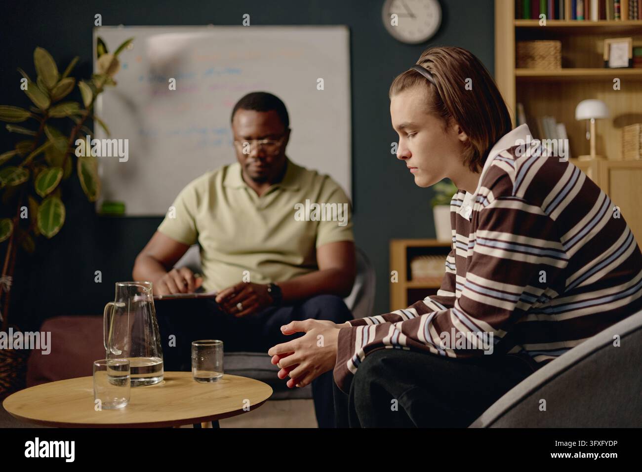 Male Teenager Talking with Black Male Psychologist during Therapy Session Stock Photo