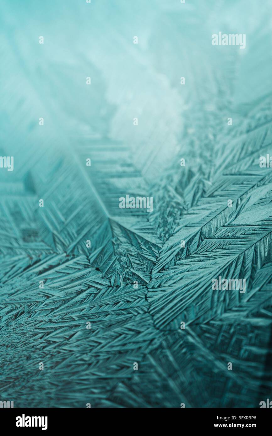 High-quality vertical macro photograph of sharp ice crystals forming a feather-like, geometric frost structure on glass. The teal and cyan gradient wi Stock Photo