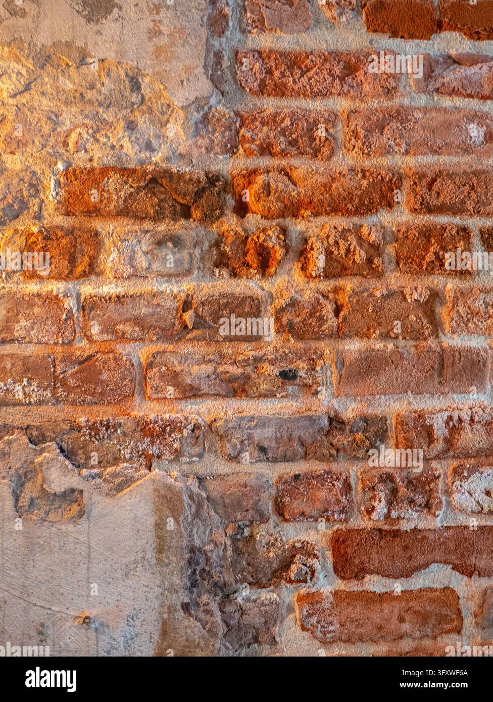 A close-up shot of an aged, weathered brick wall with exposed red bricks and patches of crumbling plaster, highlighting rustic architectural textures Stock Photo