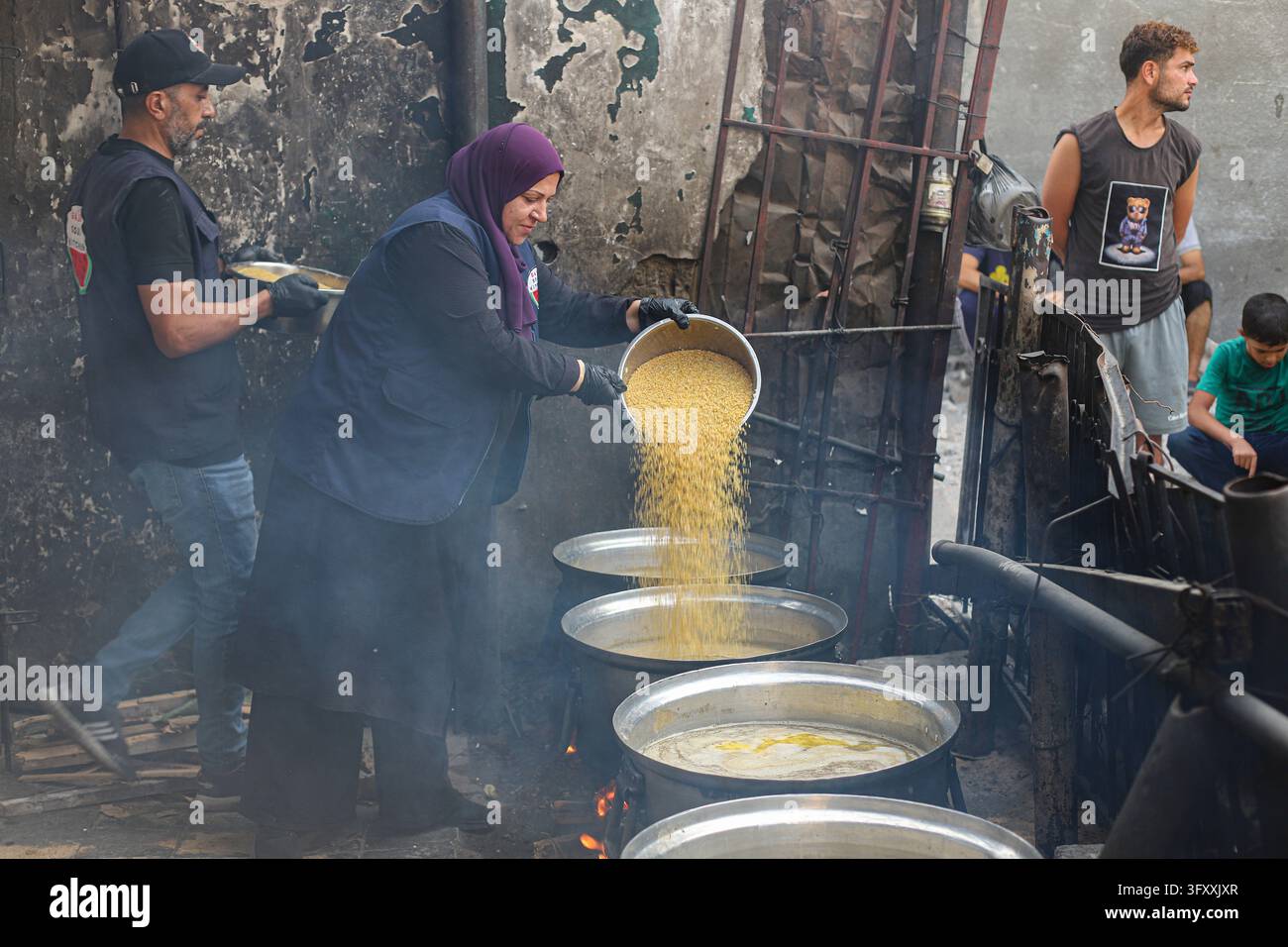 A woman pours a large quantity of cooked food from one metal vessel ...